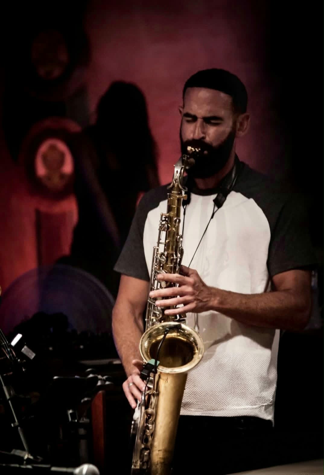 Roy Rosenberg playing saxophone on stage, lit in red.